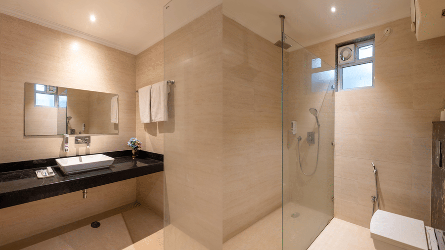 Bathroom designed with a neutral colour palette, featuring a glass-enclosed shower cabin, a rectangular washbasin, and a wall-mounted water heater above the vanity at Hotel Corporate Suites