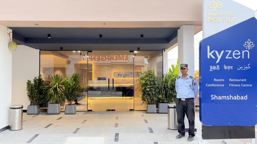 Exterior view of Kyzen hotel in Shamshabad showcasing its modern multi-storey facade, large windows, landscaped entrance, and blue hotel signage.