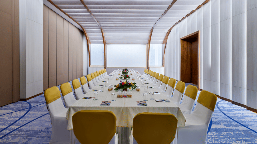 The Mahari Courtyard hall at Swosti Premium Beach Resorts, Puri, with a tablecloth and chairs in a modern venue with a distinctive curved ceiling structure.