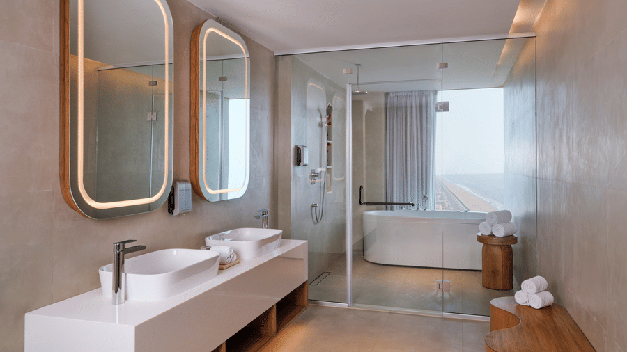 The Oasis Suite bathroom at Swosti Premium Beach Resorts, Puri, with double sinks, two large mirrors, and a bathtub along with a showerhead.