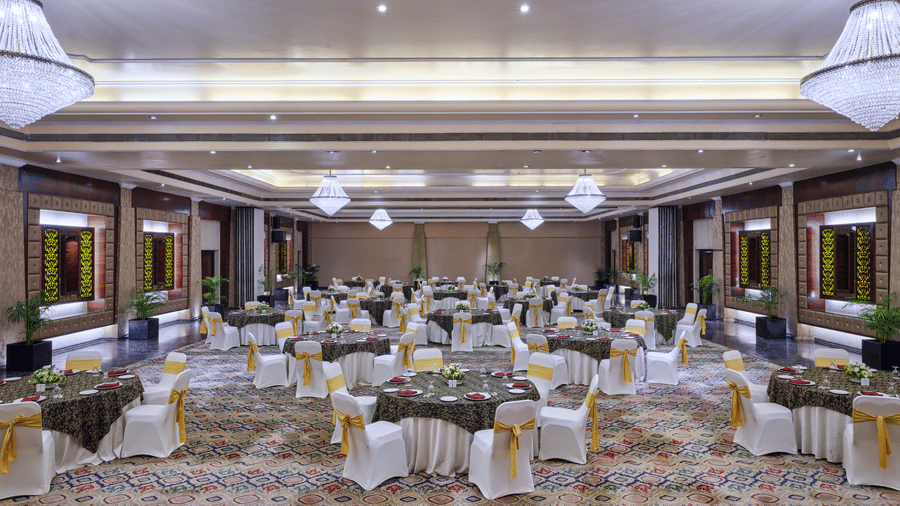 The well-lit Chanakya Banquet at Swosti Premium, Bhubaneswar, featuring chairs, tablets, chandeliers, and windows.