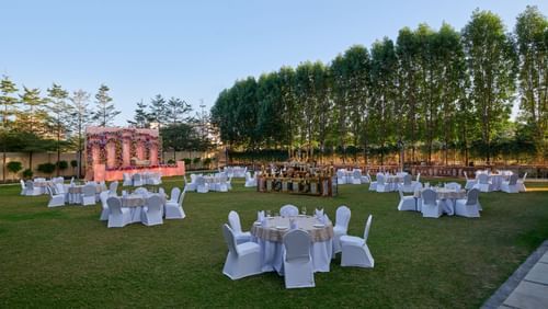 An outdoor lawn with tables and chairs with trees on the side at Tulip Inn, Bhopal.