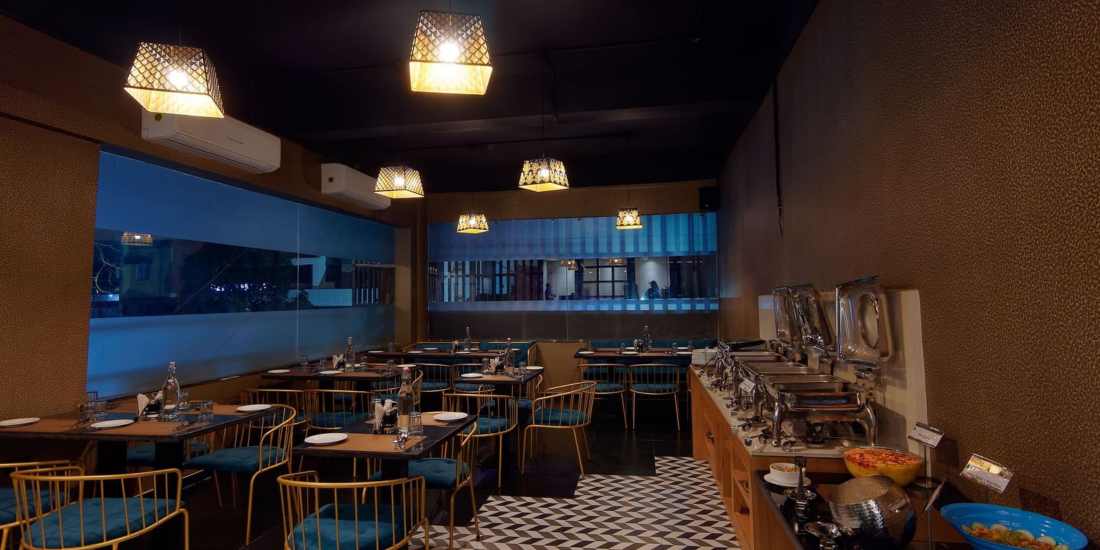 Interior of M Cafe with chairs and tables and lights hanging from the ceiling at Ankit Hotel, Jabalpur