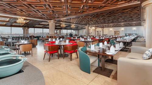 An image of our restaurant in Srinagar with high ceilings made of wooden ascents and spacious dining arrangement - Sarovar Premiere, Srinagar 