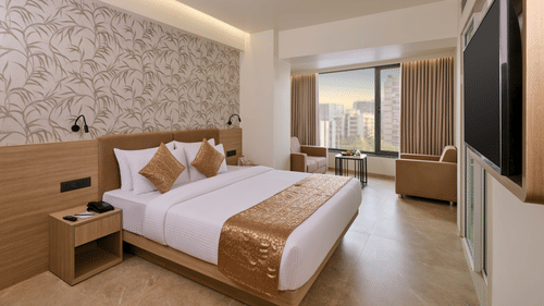 A Suite room featuring a plush bed, accent wallpaper, armchair, and a window with city view at Biznotel by Pride Motera, Ahmedabad.