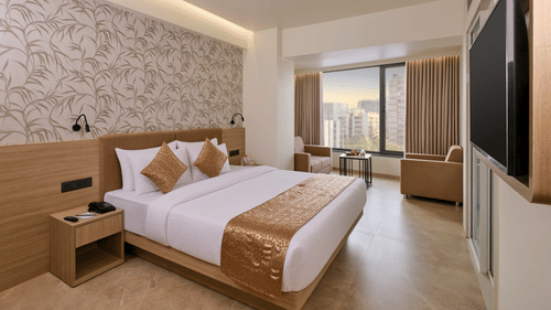 A Suite room featuring a plush bed, accent wallpaper, armchair, and a window with city view at Biznotel by Pride Motera, Ahmedabad.