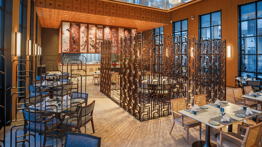 Wide view of Chin Chin restaurant at The Residency Signature Madurai with dining tables, decorative partitions, and a statement chandelier.