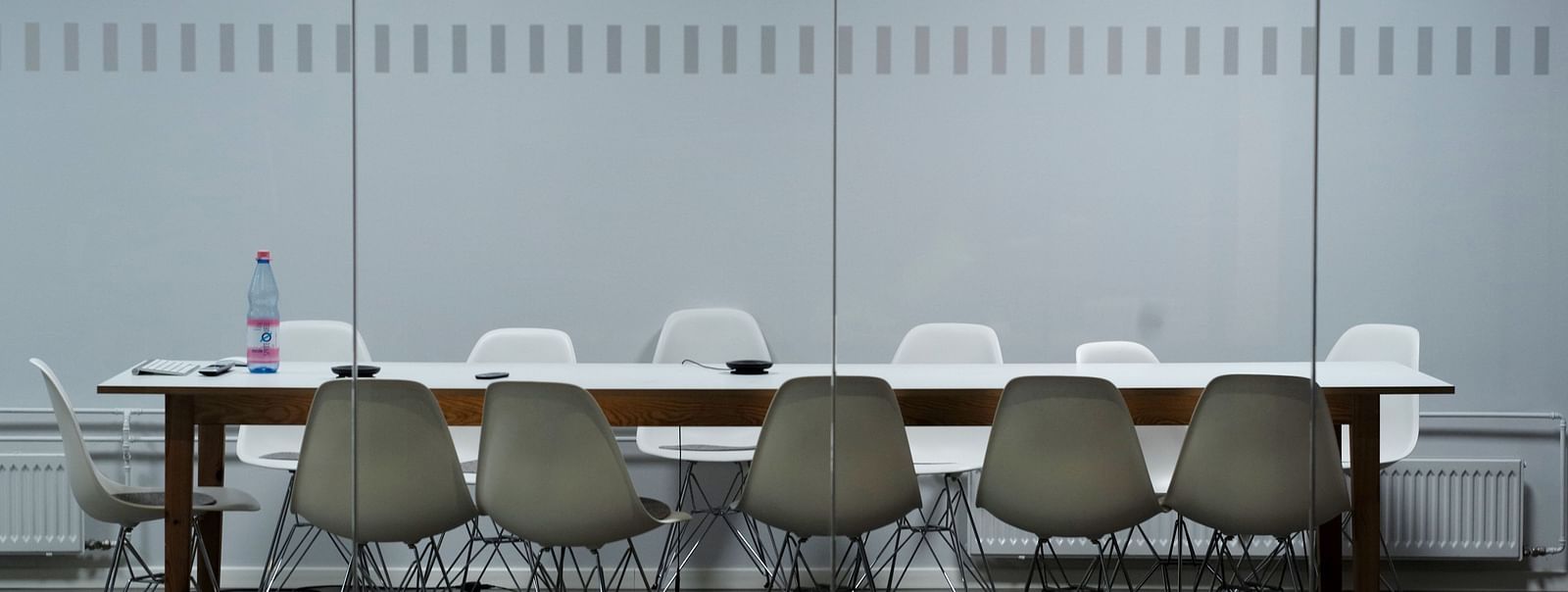 A modern meeting room with a long wooden table and a mix of white and grey chairs