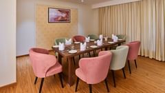 An image of a restaurant at Tulip Inn, Bhopal, showcasing a rectangular table surrounded by chairs and adorned with a chandelier overhead.