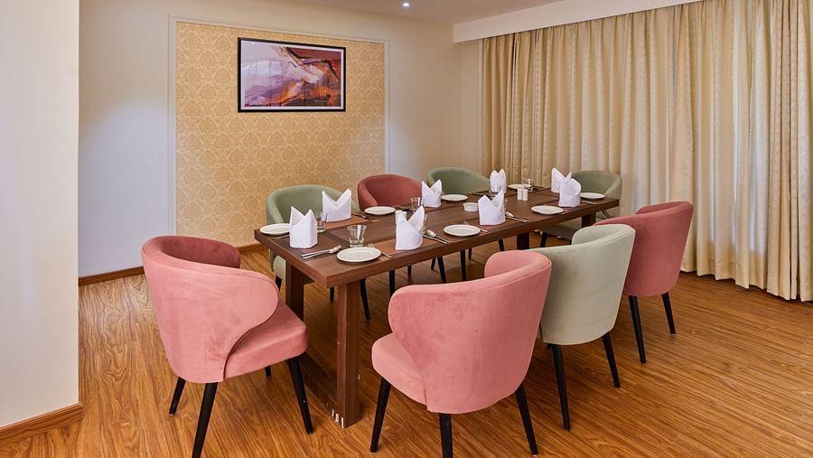 An image of a restaurant at Tulip Inn, Bhopal, showcasing a rectangular table surrounded by chairs and adorned with a chandelier overhead.