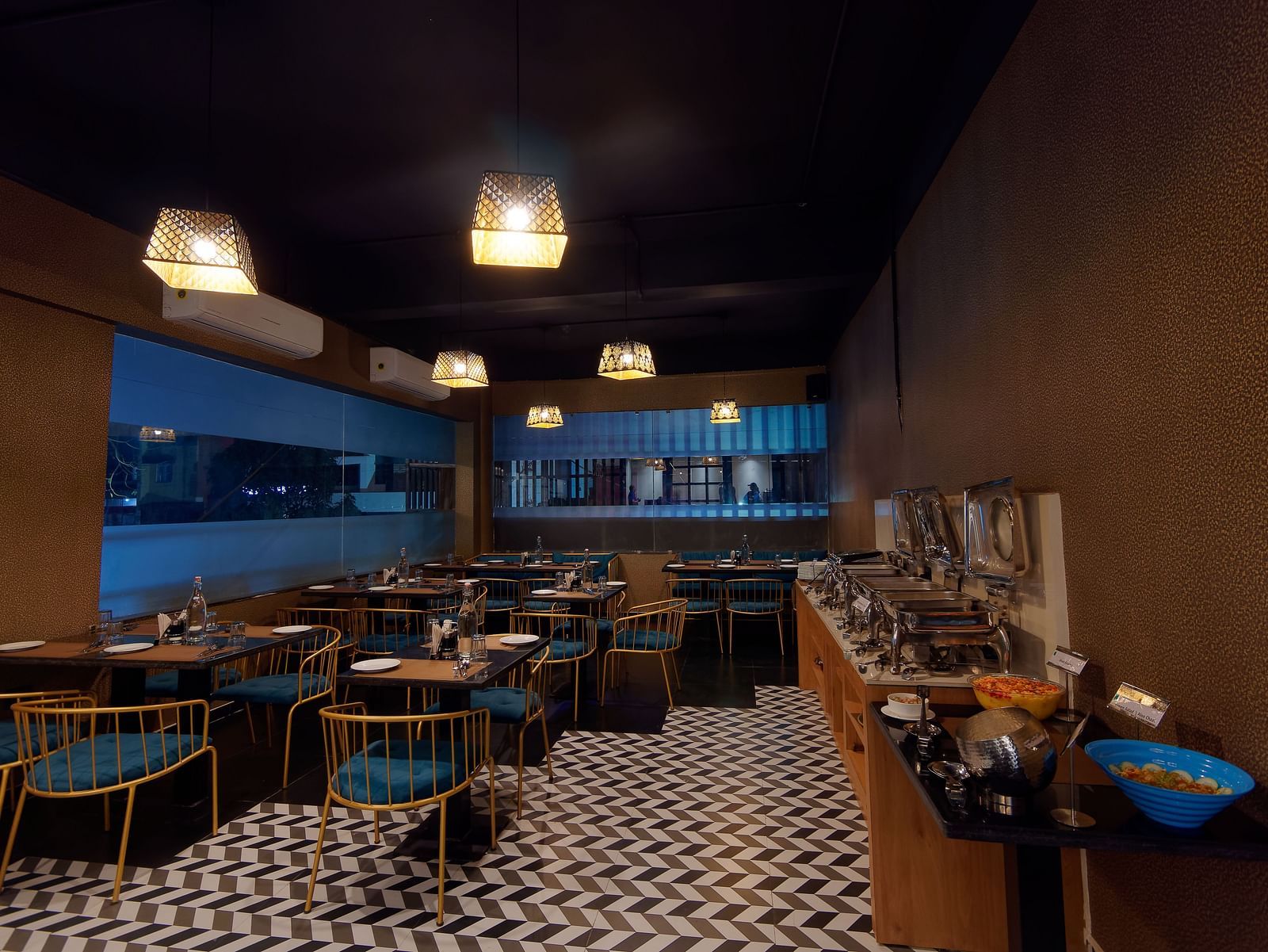 Interior of M Cafe with chairs and tables and lights hanging from the ceiling at Ankit Hotel, Jabalpur