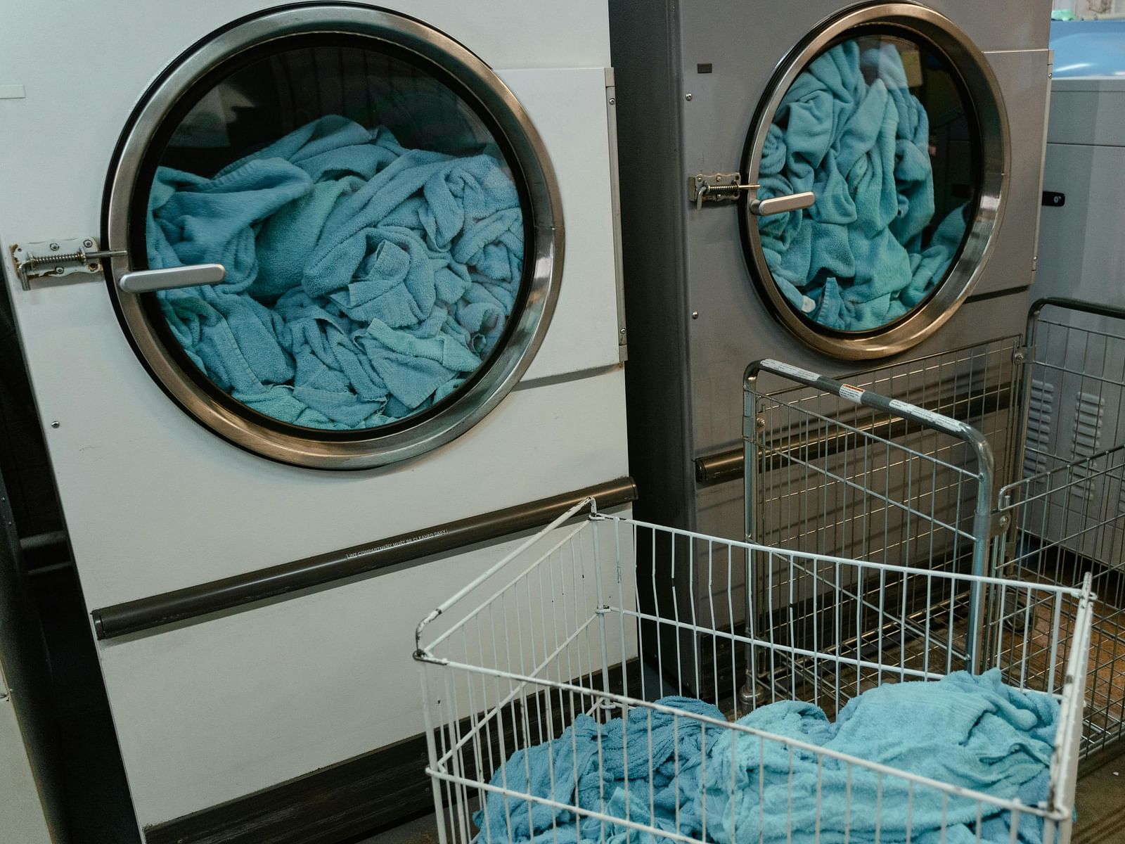 Two laundry machines with glass doors and a basket with clothes beside it