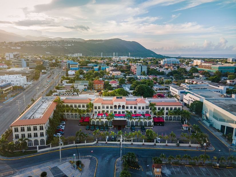 An aerial view of our hotel surrounded by lush greenery and a majestic mountain in the background, overlooking the sea - S Hotel Kingston, Jamaica