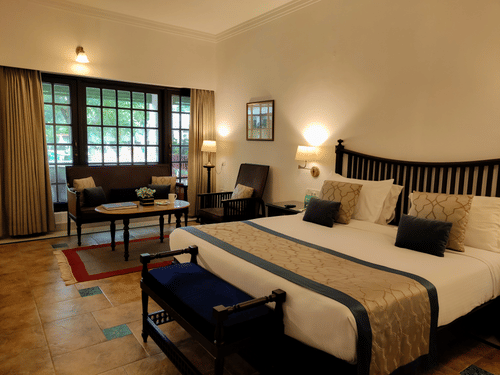 A bedroom at Jehan Numa Palace featuring a large bed with a patterned runner, warm wall-mounted lamps, and a seating area near a large window.