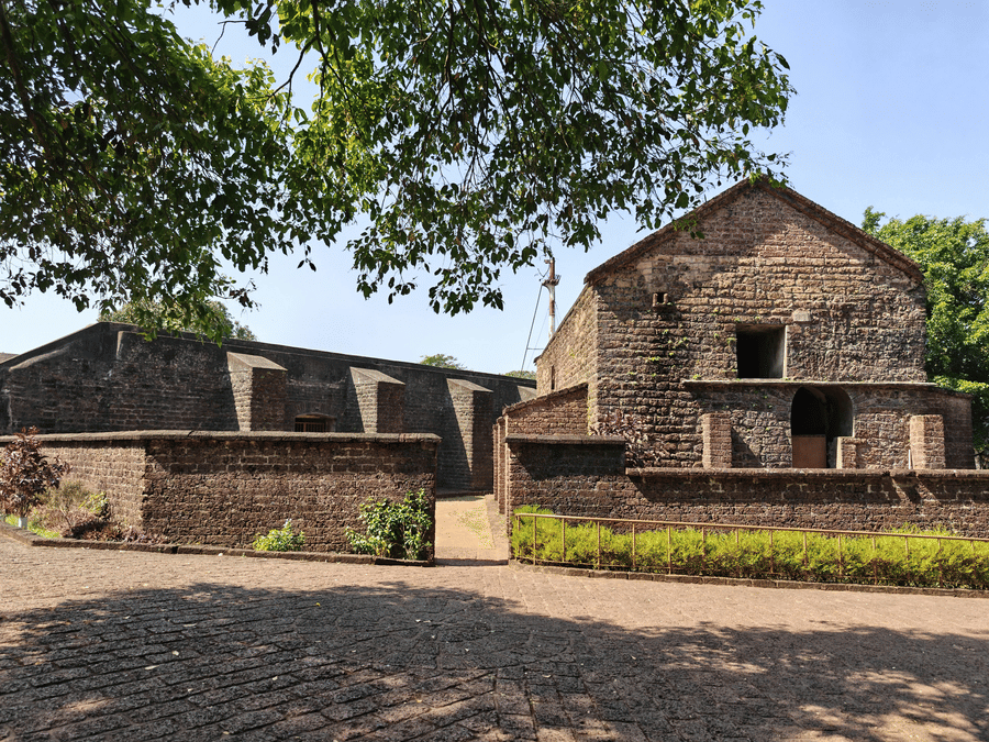 Exterior of a historic stone building under the shade of large trees.
