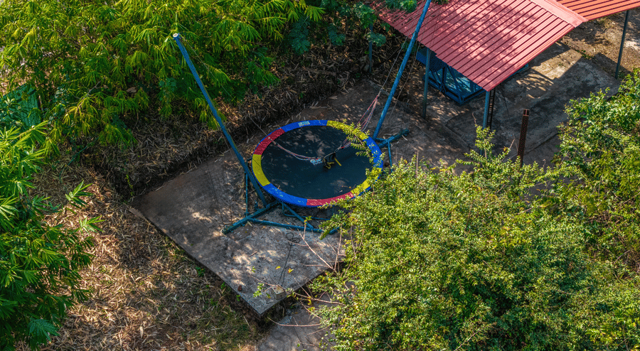 A trampoline and play equipment set up in a garden surrounded by trees.