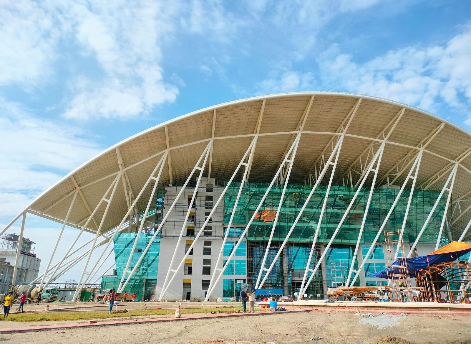 A large, modern building with a curved white roof structure against a partly cloudy sky.