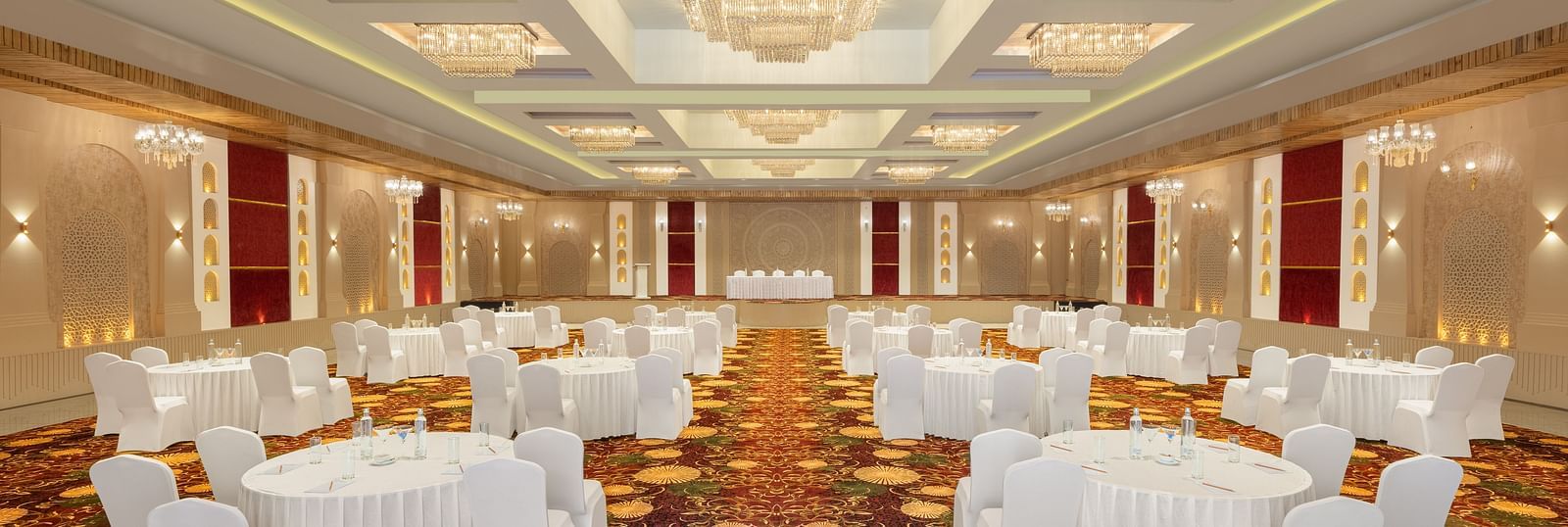 Grand Ballroom banquet setting with white chairs and tables facing the stage at Essentia Luxury Resort & Spa, Udaipur.