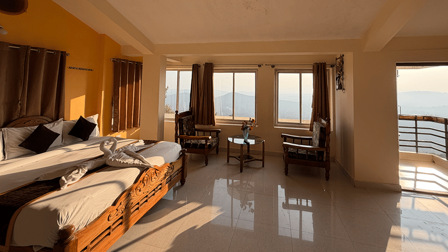 A spacious suite bedroom featuring a double bed, a seating area, and windows looking out towards hills | Kollanoor Guest House, Coorg