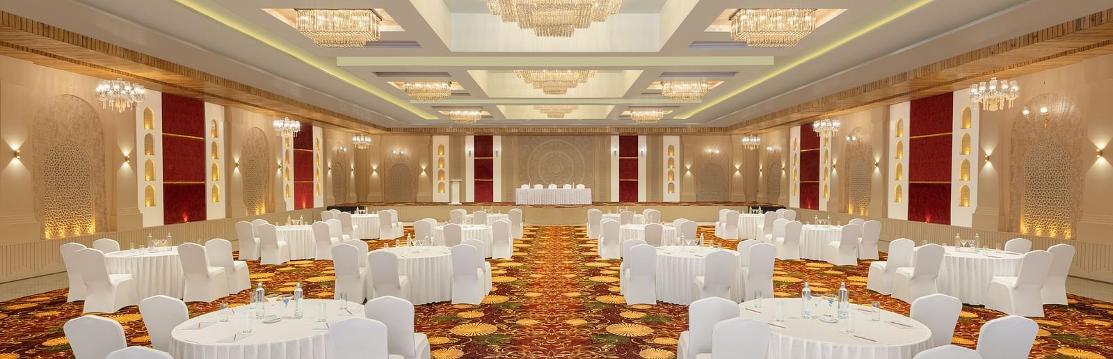 Grand Ballroom banquet setting with white chairs and tables facing the stage at Essentia Luxury Resort & Spa, Udaipur.