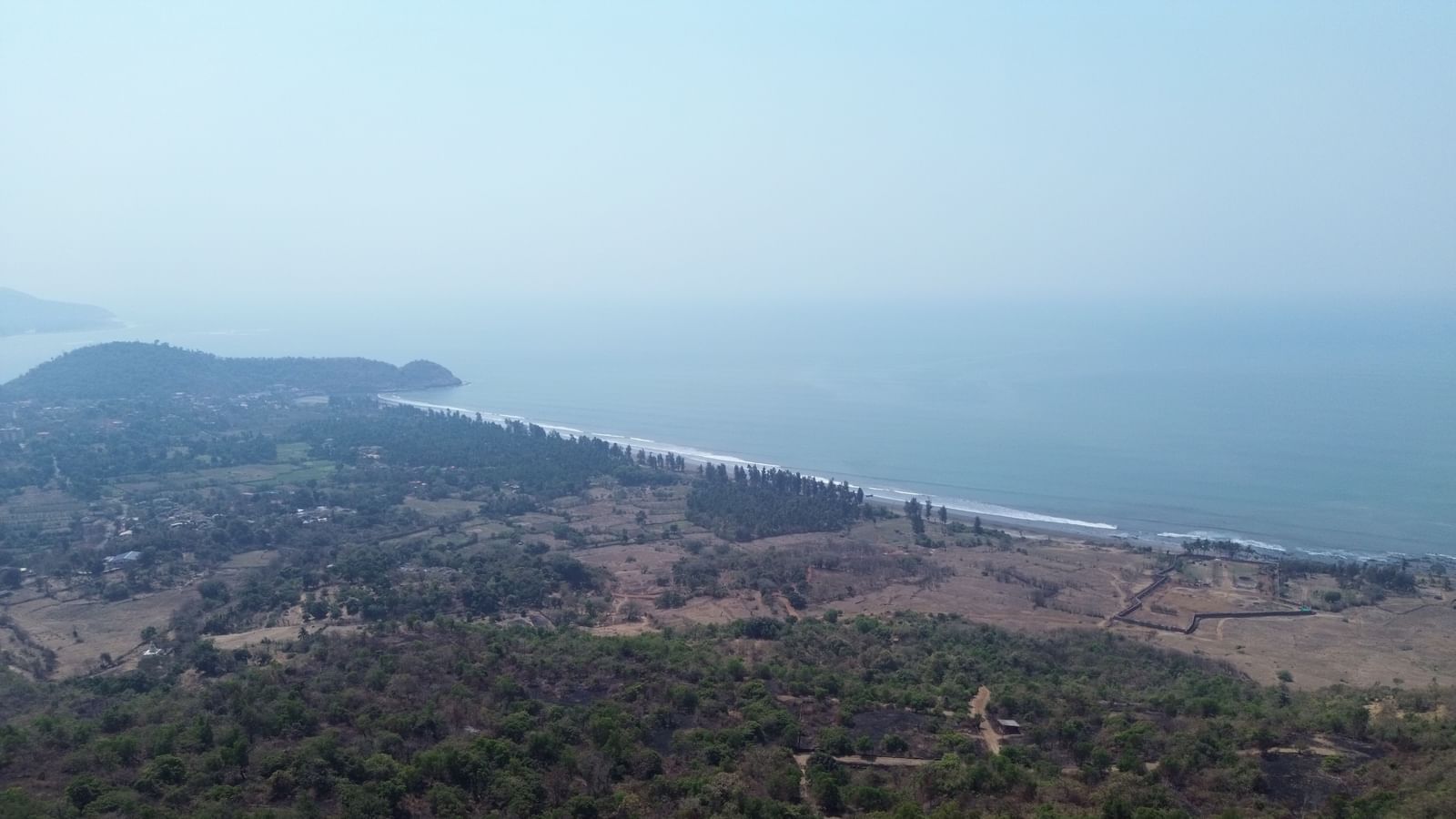 An aerial shot of a coastal landscape with green fields, a stretch of beach, and sea - Diganta