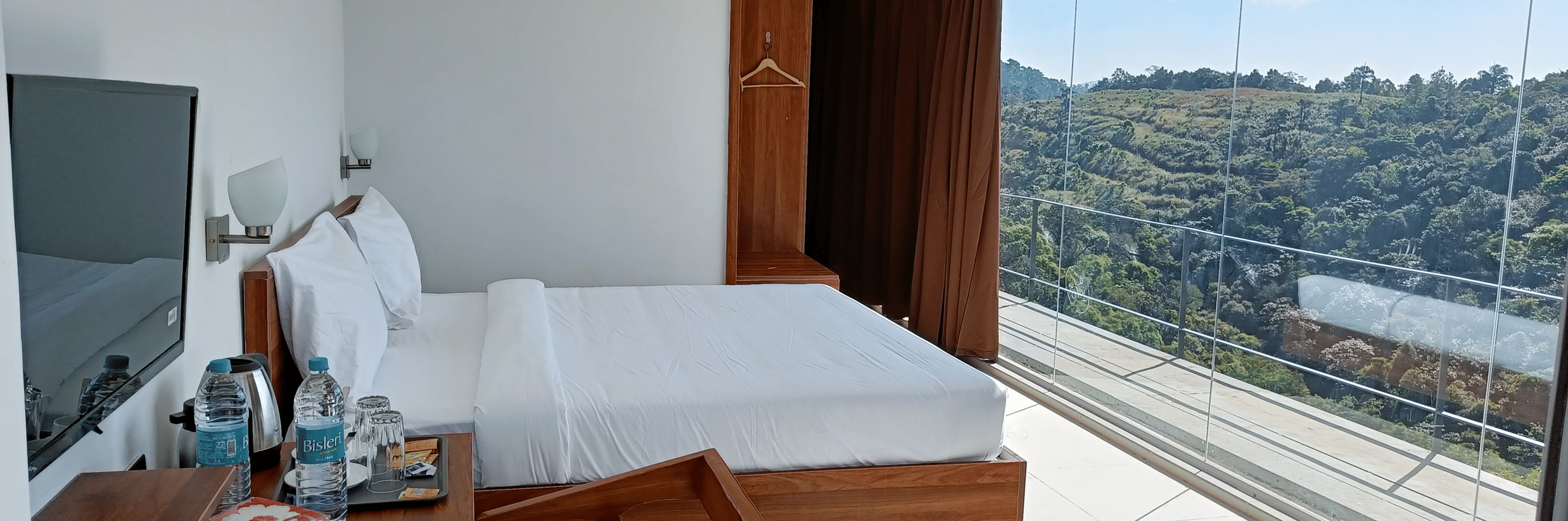 Second Floor Corner Room at The Cliff Edge Coorg Hotel featuring a bed, TV, and a work desk, with panoramic forest views visible through massive floor-to-ceiling windows.