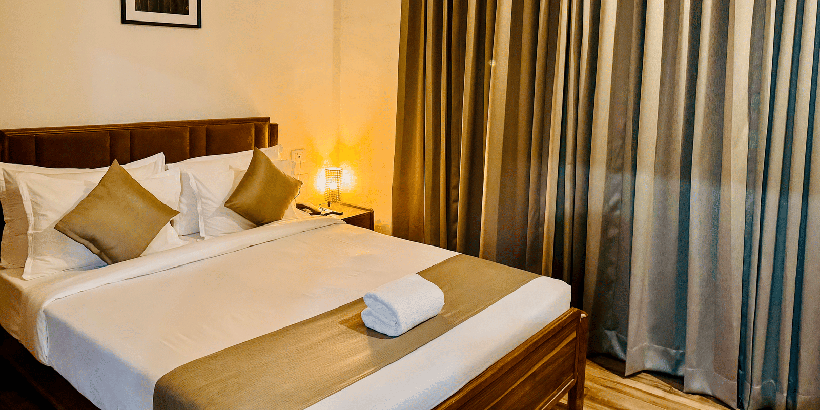 Diagonal view of the bedroom of Coral 4BHK showcasing its plush bedding, warm lighting, and closed curtains | Kove Smart Stays