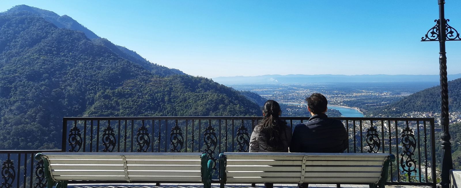 a couple sitting on a bench looking at the mountain and valley below - neer ganga Resorts