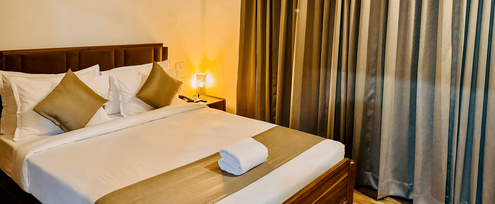 Diagonal view of the bedroom of Coral 4BHK showcasing its plush bedding, warm lighting, and closed curtains | Kove Smart Stays