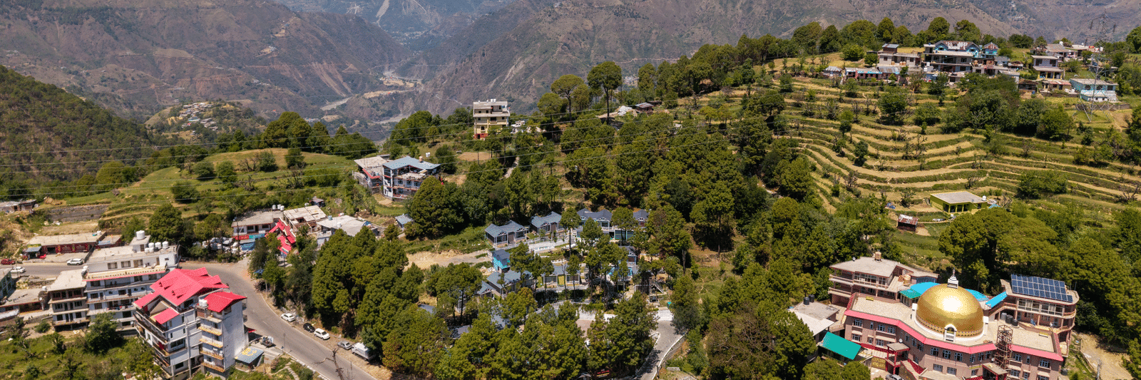 An aerial view of rolling hills, with residential and commercial buildings among lush greenery - DLS Nature Trinket Resort, best location to stay in Dalhousie.