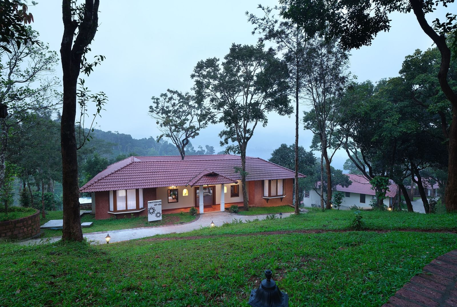 A serene view of an illuminated cottage in a lush greenery setting