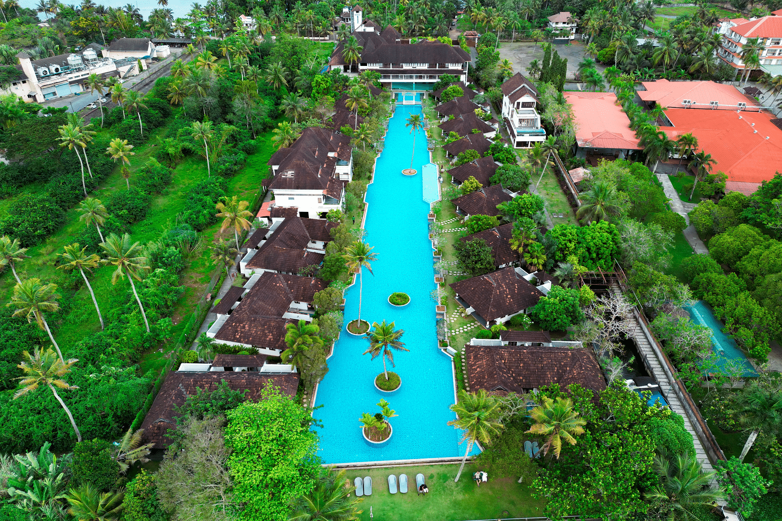 Aerial view of a Swimming pool with rooms by the side and trees behind them - Rhythm Kumarakom.