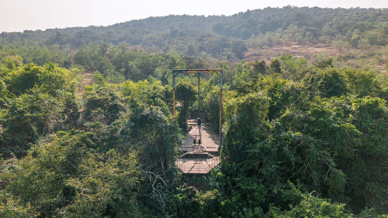 A view looking down at a tall metal structure hidden amongst green trees.