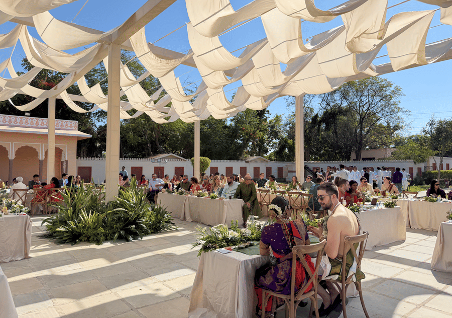 An outdoor wedding reception setup at Umaid Palace featuring long banquet tables arranged under a large, flowing white fabric canopy structure.