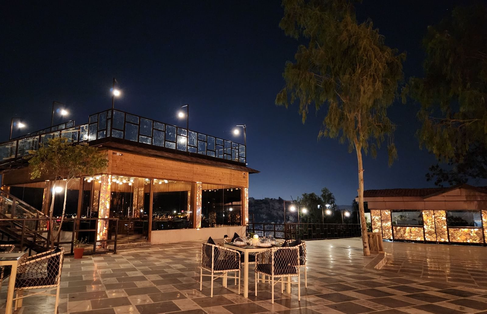 An outdoor dining area at night with a table and chairs set on a paved patio. - Bamboo Saa Resort & Spa, Udaipur