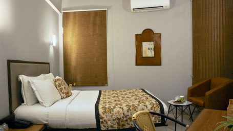 orchid room 28AOrchid Room at Polo Resort Cherrapunji with a double bed, upholstered headboard, framed traditional artwork, bamboo blinds, wall-mounted A/C and a wicker chair.