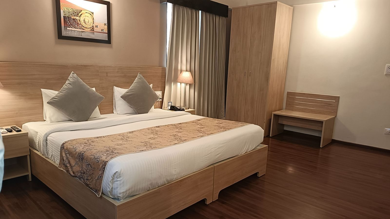 A double bed with a painting hung above inside premium studio - Starlit Suites, Shirdi
