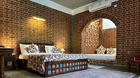 Bedroom with double bed, patterned bedding, and arched brick window at Tisya Farms, Gurgaon.
