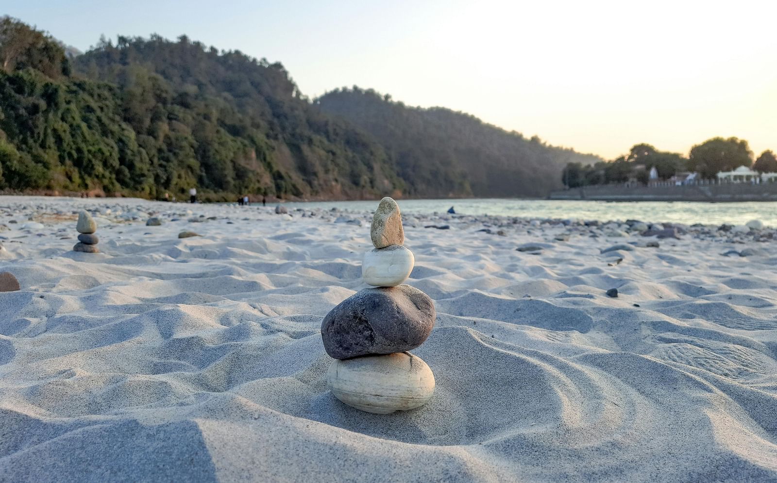 An image of pebbles placed on a sandy area with lush green mountains in the background.