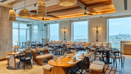 The well-lit Beach Hut at Swosti Premium Beach Resorts, Puri, featuring wooden accents, multiple dining tables, and large windows. 
