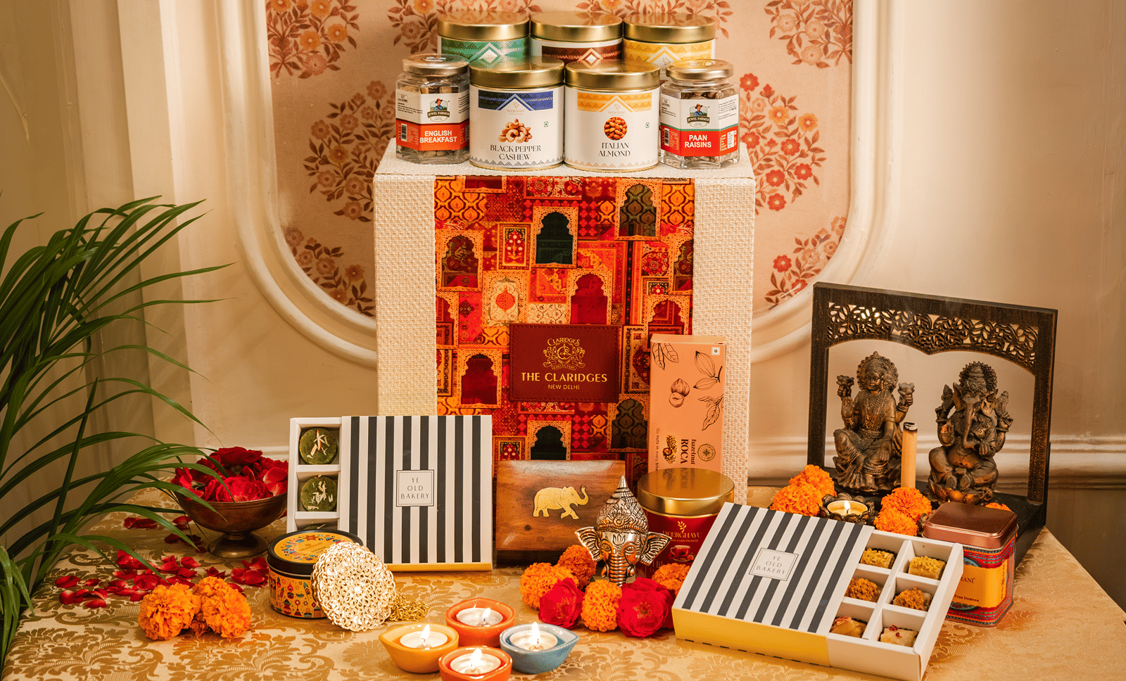 A Diwali Hamper from the Claridges Collection New Delhi featuring boxes of sweets, dry fruits, a small idol of Gods decorated with flowers, and more.