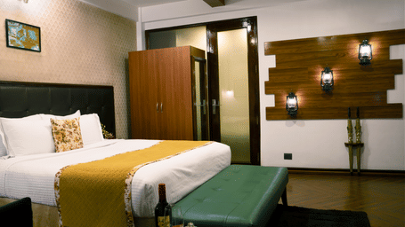 Suite bedroom at Polo Resort Cherrapunji with king bed, yellow throw, lantern wall lights, wardrobe, green ottoman and Sula wine on a side table.