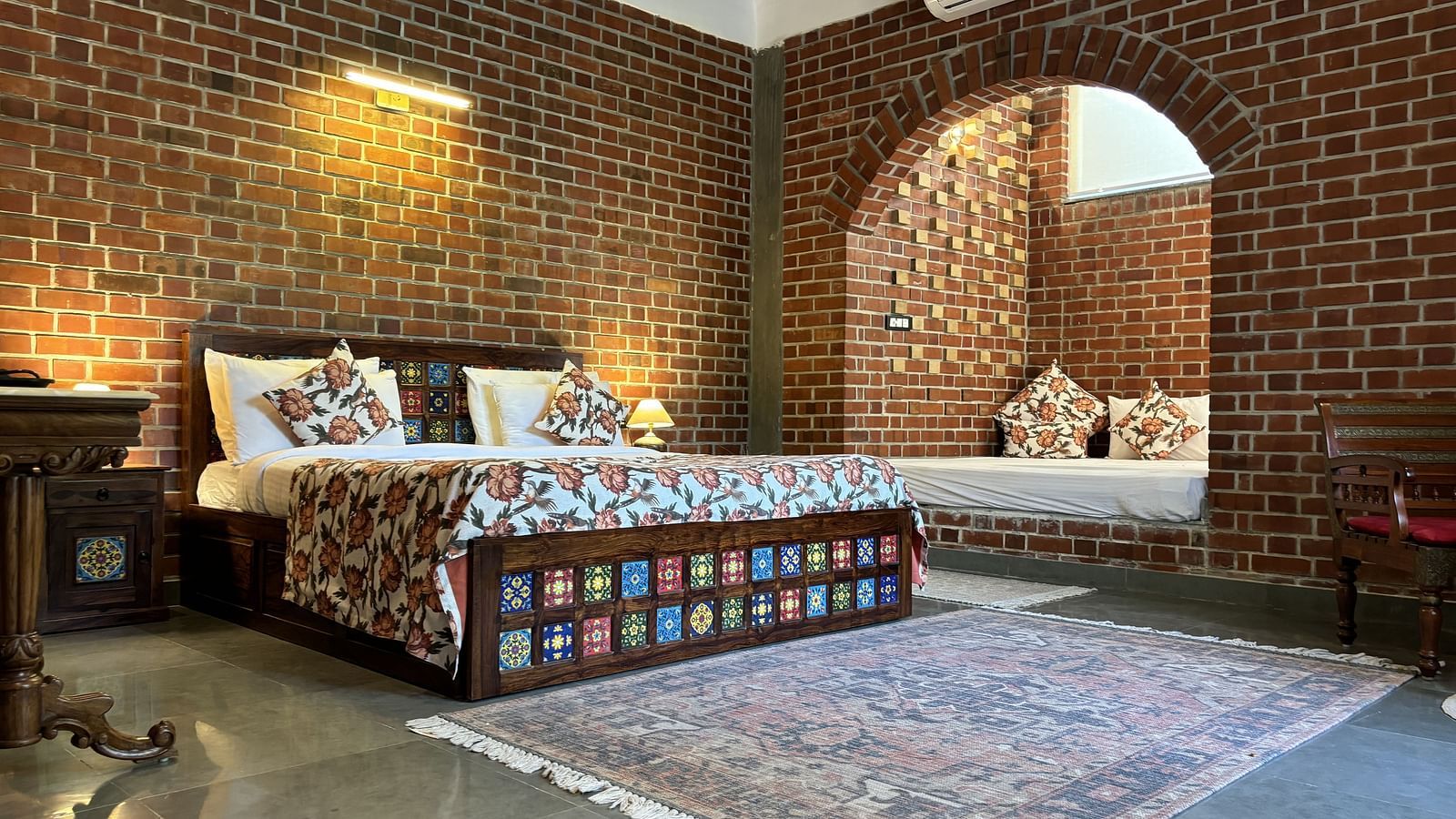 Bedroom with double bed, patterned bedding, and arched brick window at Tisya Farms, Gurgaon.