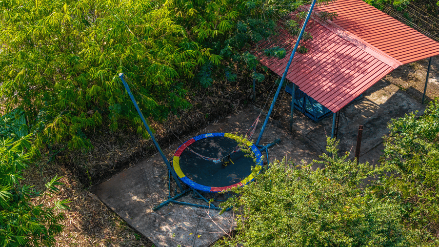 A trampoline and play equipment set up in a garden surrounded by trees.