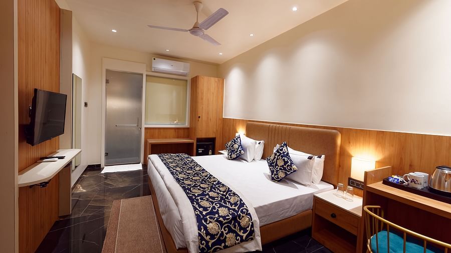 Image of deluxe room with a bed with table and chair on the side of the table and a fan on te ceiling at Ankit Hotel, Jabalpur