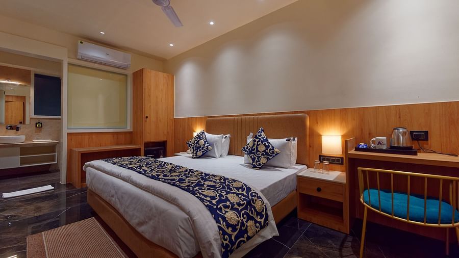 Image of studio room with a bed with table and chair on the side of the table and a fan on te ceiling at Ankit Hotel, Jabalpur