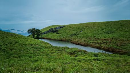 Scenic valley with rolling green hills and a small river under a cloudy sky.