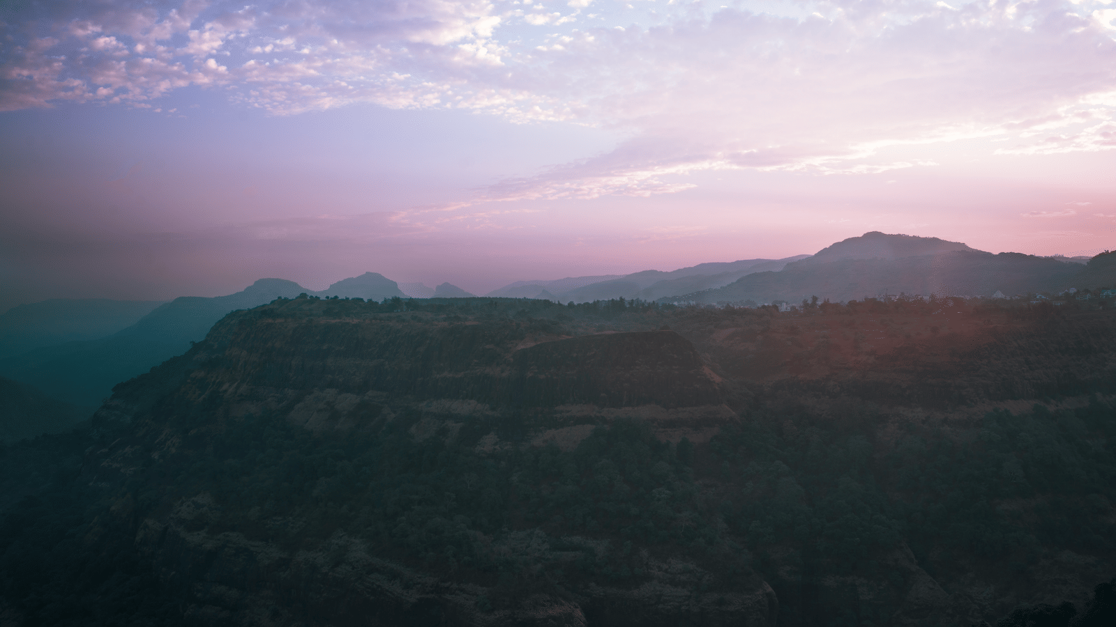 An aerial view of rolling hills and mountains shrouded in mist during a colourful sunrise or sunset at Athiva Hotels & Resorts.