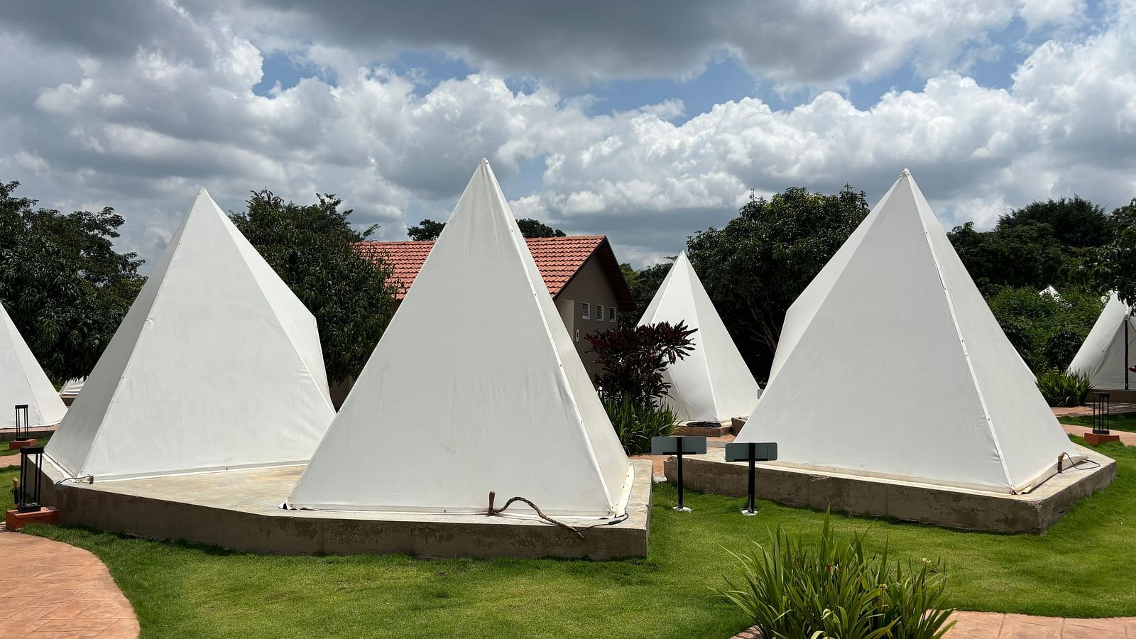 A scenic view of a resort area with tents lined along a neat walkway, surrounded by a well-maintained lawn.