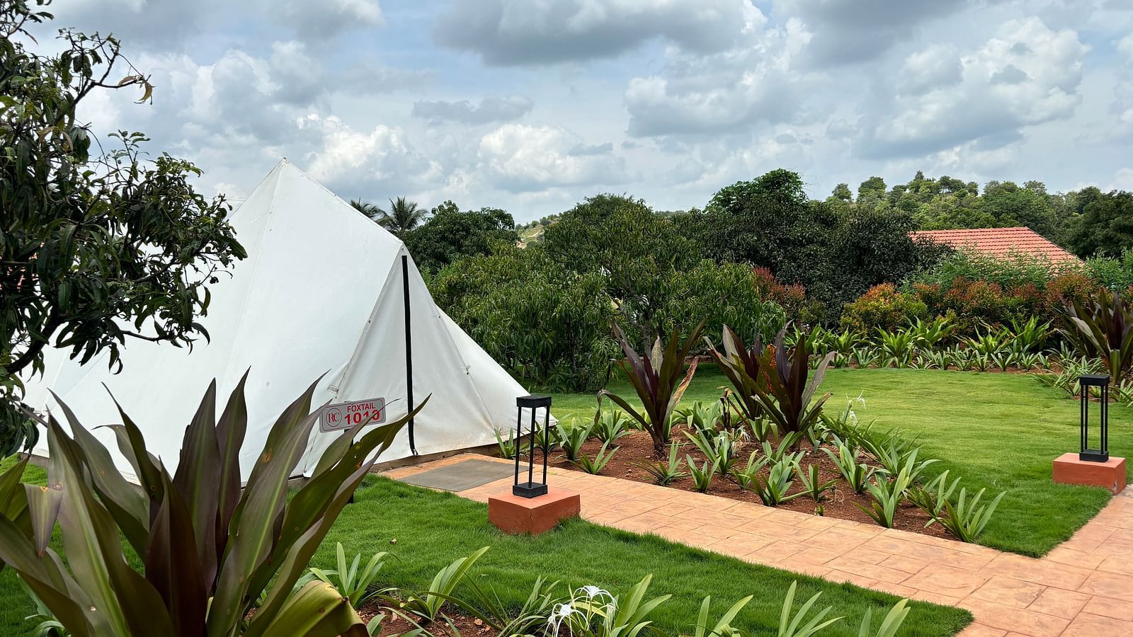 A scenic view of a resort area with tents lined along a neat walkway, surrounded by a well-maintained lawn.